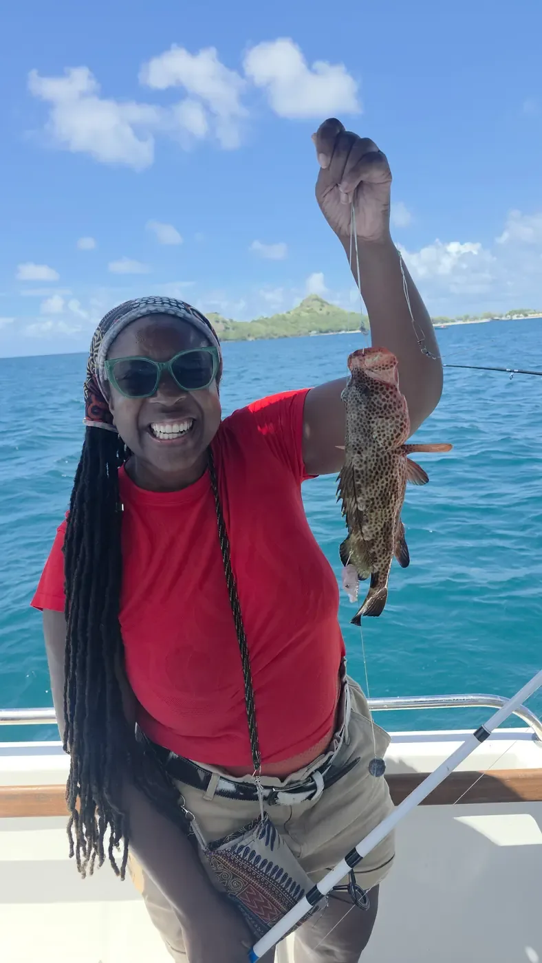 A smiling guest holding up a spotted red hind on the boat